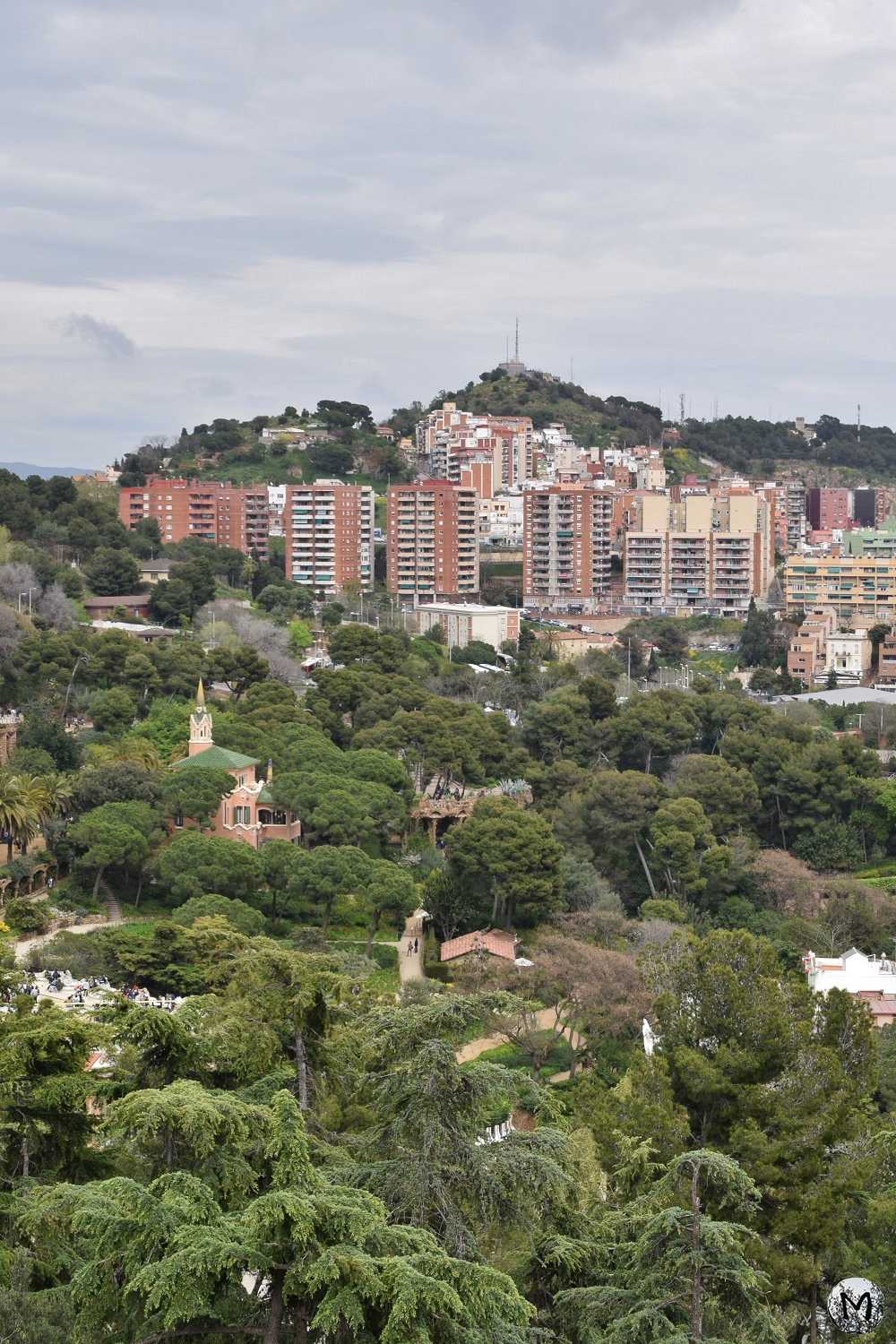 Vue sur la végétation luxuriante du Parc Güell à Barcelone, avec des immeubles à l'arrière.