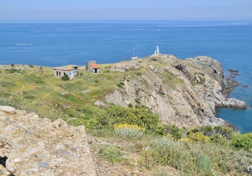 Panorama des falaises du Cap Béar avec ses monuments en ruines et ses bateaux en mer.
