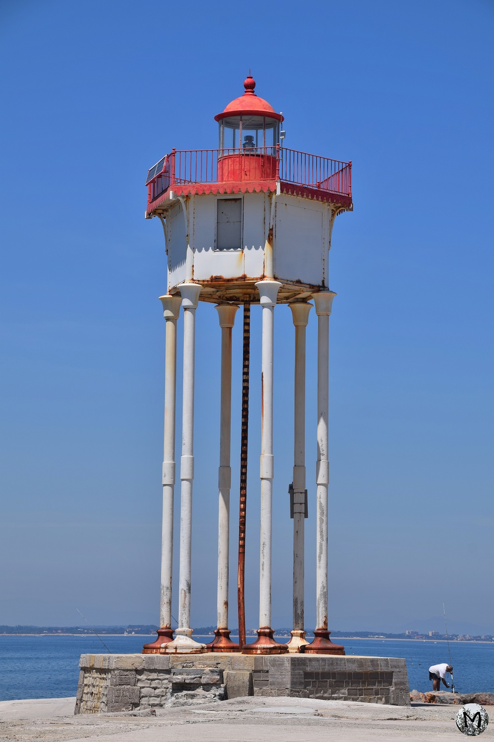 Phare et pêcheur de la jetée de Port-Vendres lors d'une journée avec un grand ciel bleu.